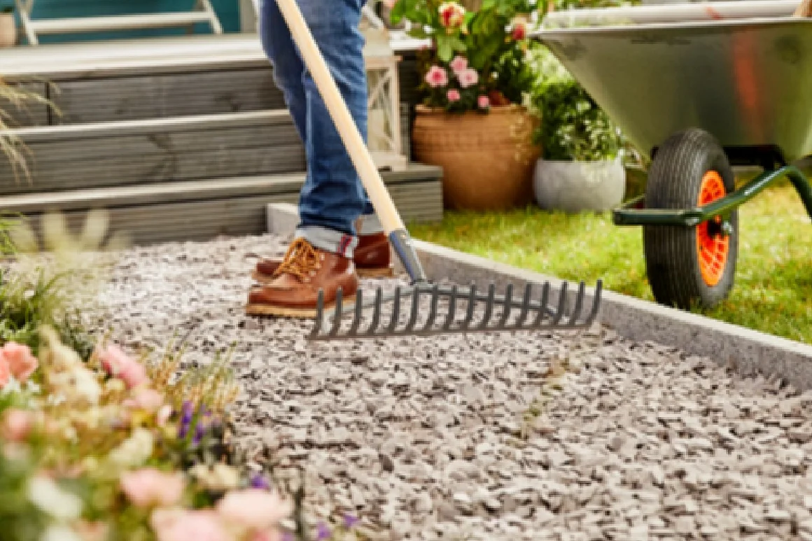 Person harkt Kiesweg im Garten